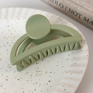 Détail de la pince à cheveux vert mat au design évidé sur un plateau en céramique blanc