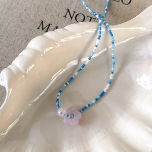Detail of beaded necklace with blue beads and a purple flower pendant on a shell tray