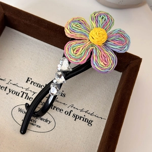 Détail macro de la pince à cheveux fleur arc-en-ciel avec strass en cœur sur base noire