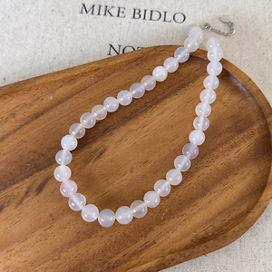 Detail view of natural white translucent agate beaded necklace on a wooden tray