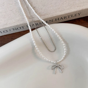 Elegante collana a due strati con fiocco d'argento e perle bianche su un vassoio di ceramica