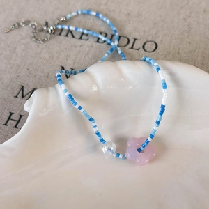 Close-up of a beaded floral necklace with pink flower charm in a shell porcelain dish
