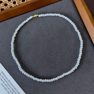 Detailed view of round white pearl necklace with golden magnetic clasp on display