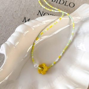 Close-up of beaded flower necklace with yellow petals and white pearl in a shell tray