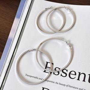 Polished silver metal hoop earrings in two sizes shown on a white artistic magazine