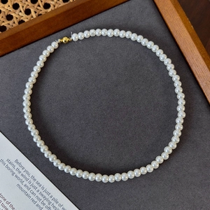 Close-up of round white pearl necklace with golden magnetic clasp on a grey surface