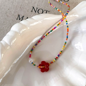 Close-up of bohemian colorful beaded choker with a red flower pendant on a shell plate