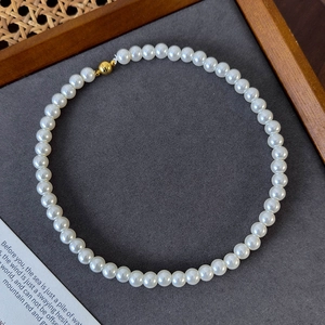 Detail of round white pearl necklace featuring a golden magnetic clasp on a grey tray