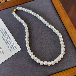 Detail of 8mm round white pearl necklace with gold magnetic clasp on grey textured board