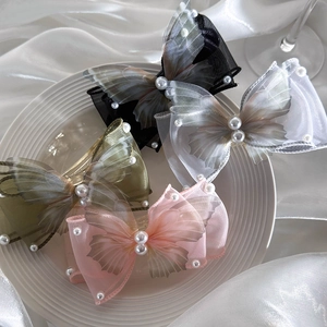 Detail of four butterfly hair clips in silk fabric with pearls on a textured white plate