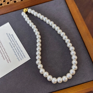 Detailed view of white round pearl necklace with golden magnetic spherical clasp