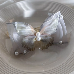 Detailed view of gray organza butterfly hair clip with white pearls on a white plate