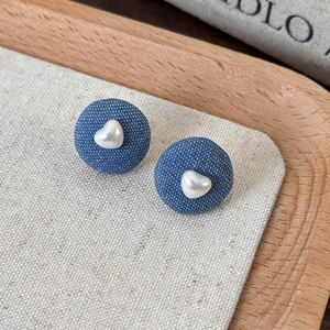 Close-up of blue denim button stud earrings with a white heart pearl on a wooden tray