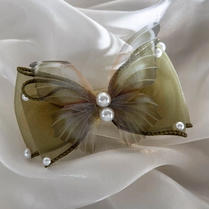 Macro view of olive green butterfly hair clip with organza layers and pearl details