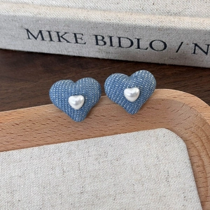 Close-up of vintage heart earrings with blue denim texture and pearl heart center decoration