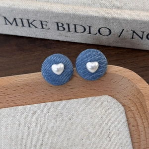 Close-up of retro blue denim round stud earrings with a white 3D heart on a wooden tray