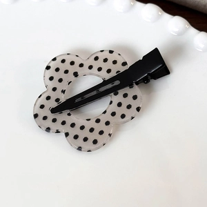 Dettaglio di un fermaglio per capelli floreale in acrilico a pois su un piatto bianco
