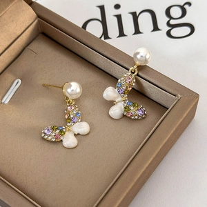 Close-up of butterfly earrings with colorful rhinestones and white pearls in a golden tray