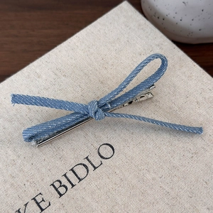 Détail d'une pince à cheveux avec nœud en jean bleu sur une base en métal argenté poli