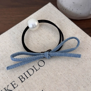 Détail macro du chouchou nœud en denim bleu avec perle blanche sur fond épuré