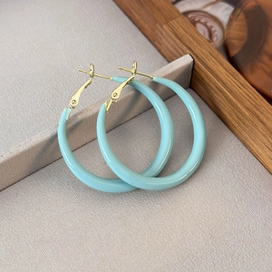 Macro detail of large light blue enamel hoop earrings with gold metal hooks on fabric