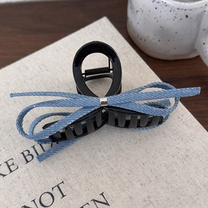 Détail d'une pince à cheveux à nœud en denim bleu avec boucle argentée sur un livre