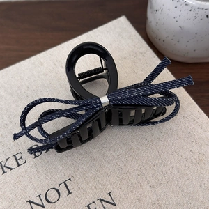 Détail d'une pince à cheveux en résine noire avec nœud en denim bleu et boucle métallique