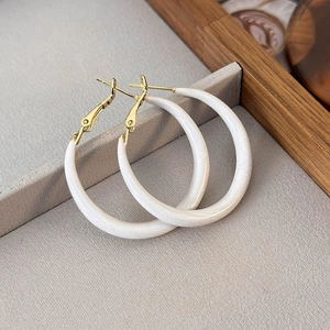 Detail shot of white enamel and gold hoop earrings on a textured display tray