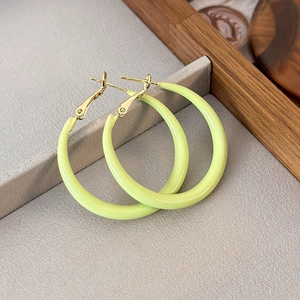 Close-up of mint green enamel hoop earrings on a grey tray with a lifestyle background