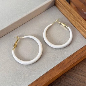 Detail view of cream enamel hoop earrings with gold metal hooks in a display box
