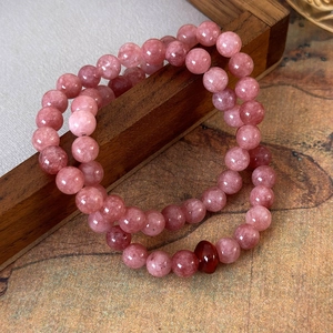 Detail of pink strawberry crystal beaded bracelets with a red accent on wood