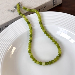 Macro view of green stone beaded necklace with silver clasp on white textured ceramic