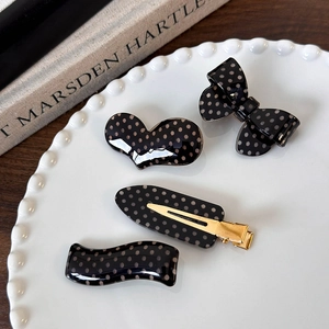 Close-up of four black polka dot hair clips in heart and bow shapes on a white plate