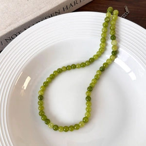 Detail of green beaded necklace with natural jade stones on a white ceramic plate