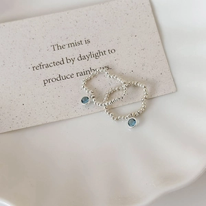 Blue crystal beaded elastic rings in silver finish on a minimalist ceramic plate