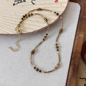 Detail of beaded necklace with gold metal tubes and tiger eye stones on a zen fan