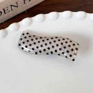 Detail of wavy resin hair clip with black polka dots on an elegant lace ceramic plate