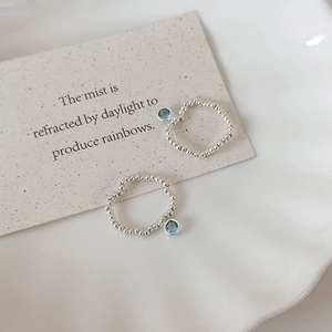 Elastic silver beaded ring featuring a hanging blue crystal charm on a decorative dish
