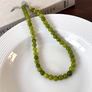 Close-up of green beaded stone necklace with silver clasp on white ceramic plate