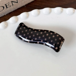 Close-up of black wave acrylic hair clip with brown polka dots on a white ceramic plate