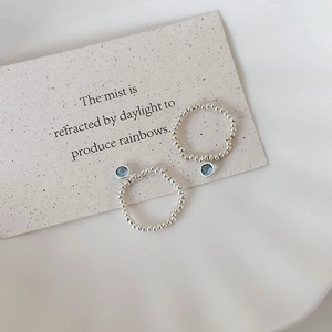 Detail of silver beaded elastic rings featuring blue crystal charms on aesthetic card