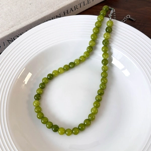 Detail of green beaded stone necklace with silver lobster clasp and extension chain on white plate