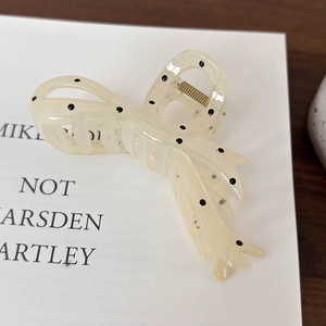 Detail of a creamy translucent hair claw clip with black polka dots and metal spring