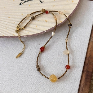 Detail of Zen style necklace featuring natural stones and amber-toned beads on white fabric