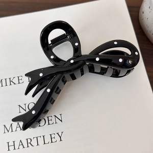 Detail view of a black hair claw clip with white polka dots and a sturdy metal spring