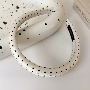 Detailed view of the padded white polka dot satin headband on a ceramic tray