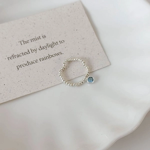 Detail of silver beaded stretch ring with a blue round crystal pendant on a white plate