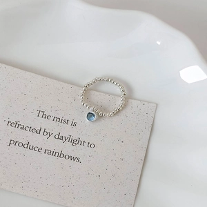 Detailed close-up of beaded silver ring with round blue gemstone charm on a tray