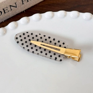 Close-up of translucent acrylic hair clip with black polka dots and gold metal clip