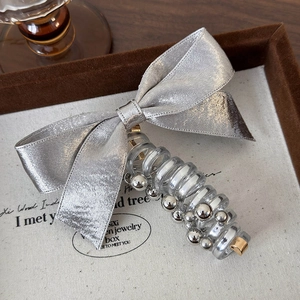 Detail of silver bow hair tie with spiral design and metallic bead accents on a beige background